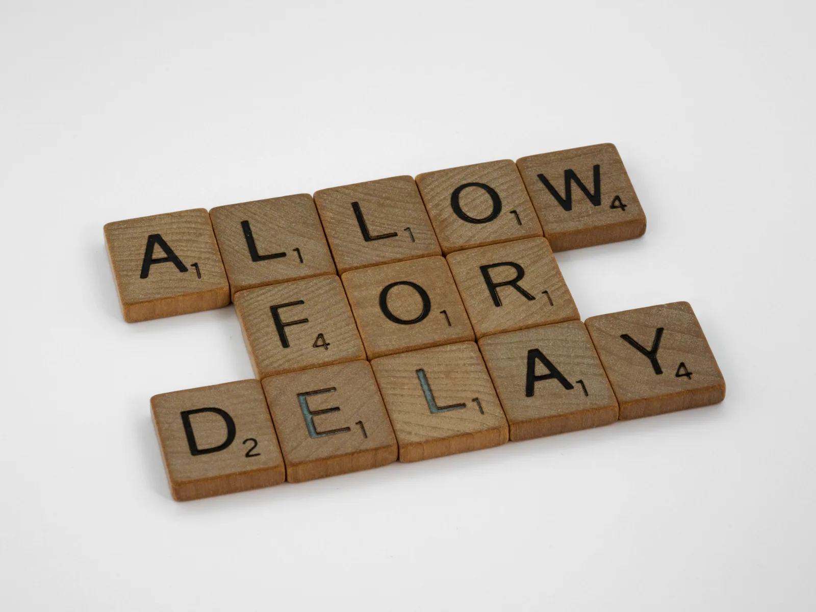 Wooden letter tiles on a white background spelling 'Allow for Delay'.