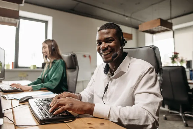 Two professionals in an office wearing headsets, engaging in friendly teamwork. Software per il servizio clienti